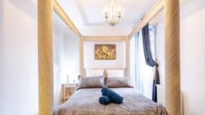 A bedroom with a bed, a chandelier, a painting on the wall, and a window with curtains. - Escapade Exotique-Private Terrace-Love&Jacuzzi (Franconville)