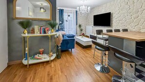 A modern living room with a large mirror, a blue sofa, a coffee table, and a dining area with bar stools. - Escapade Exotique-Private Terrace-Love&Jacuzzi (Franconville)