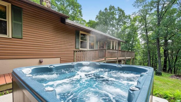 Ein Whirlpool vor einem Holzhäuschen mit einer Terrasse, umgeben von Bäumen.