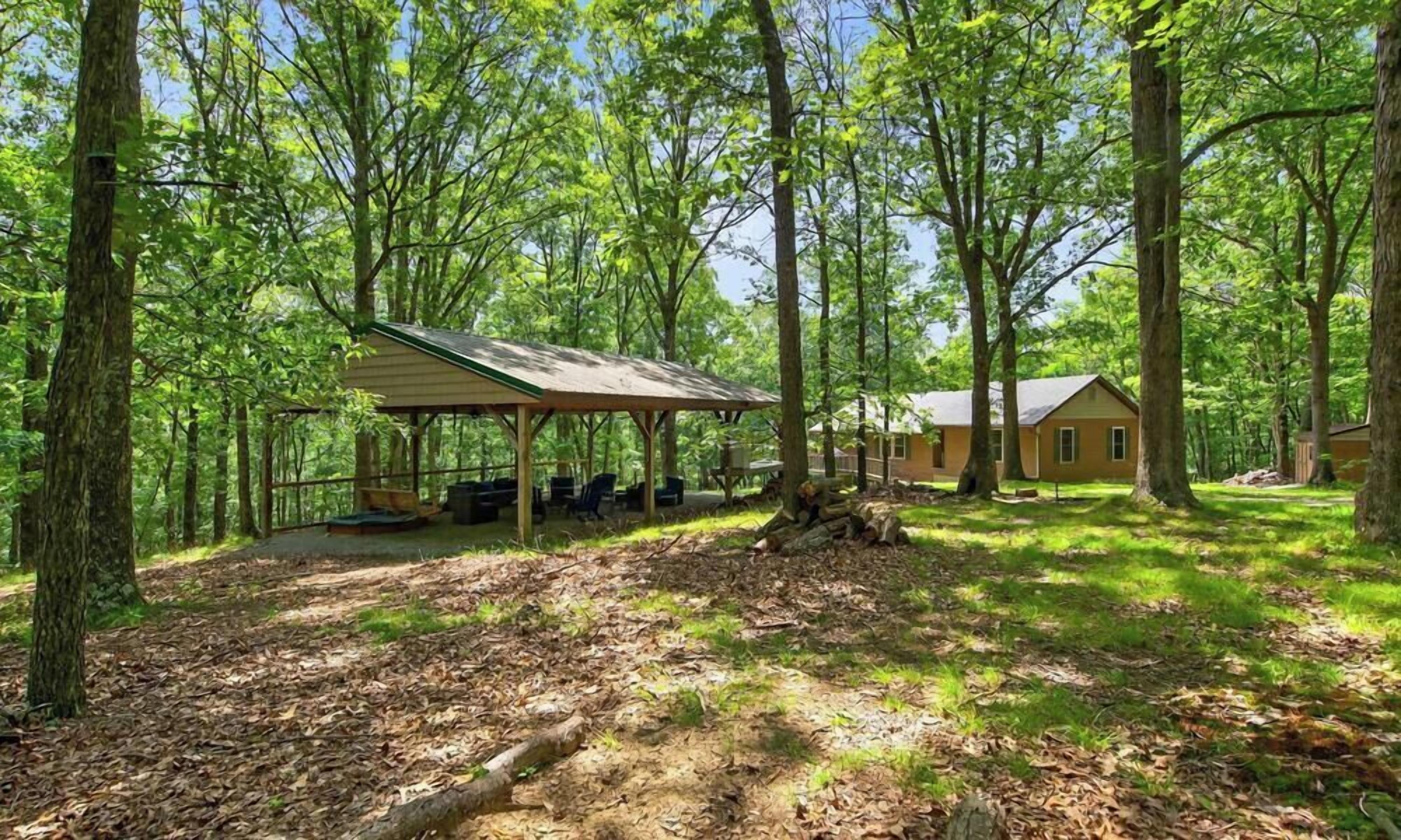 A wooded area with a covered pavilion and a cabin.