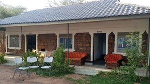 Um edifício de dois andares com telhado de telhas, cozinha e área de recepção. Há cadeiras ao ar livre e um pequeno jardim.