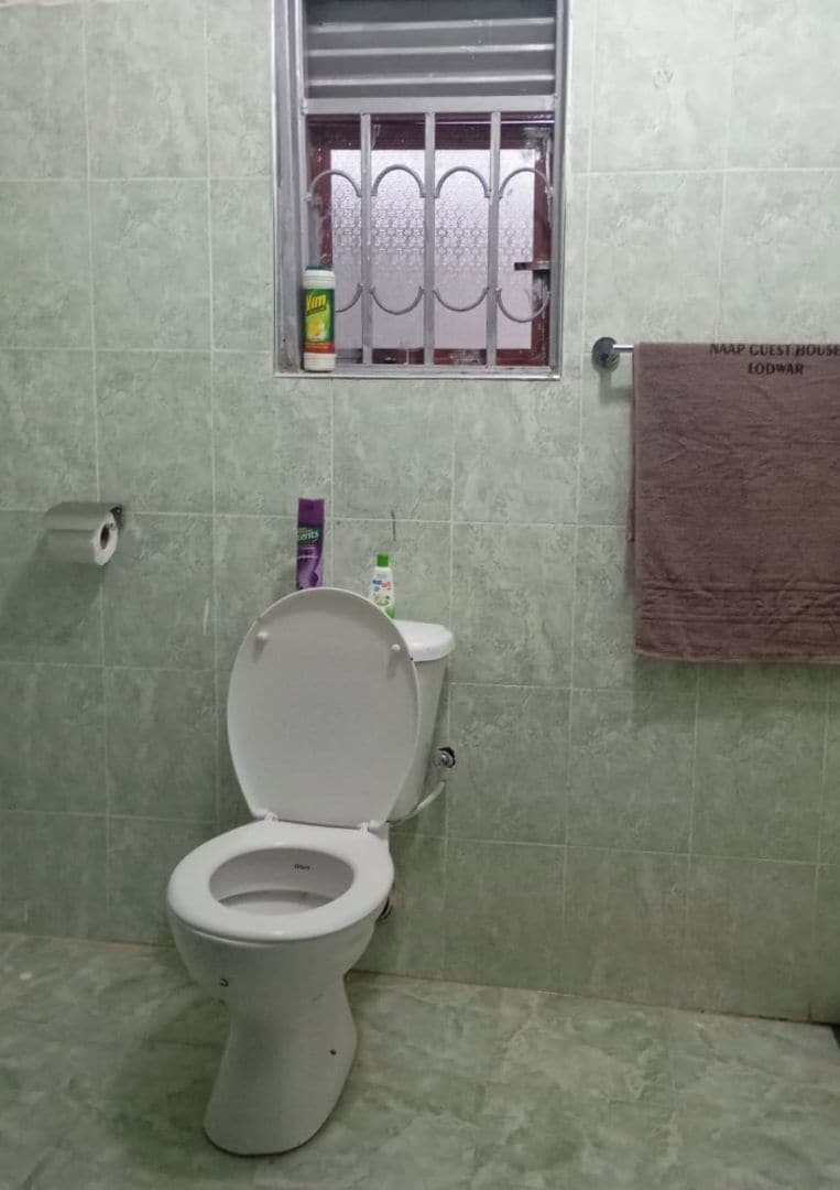 A bathroom with a toilet, a window with bars, a towel hanging on the wall, and a toilet paper holder.