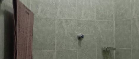 A bathroom with green tiles, a showerhead, a towel rack, and a faucet.