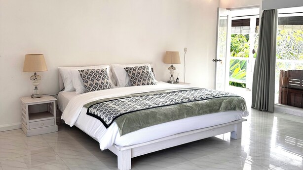 Um quarto espaçoso com uma cama grande, paredes brancas e um ventilador de teto.