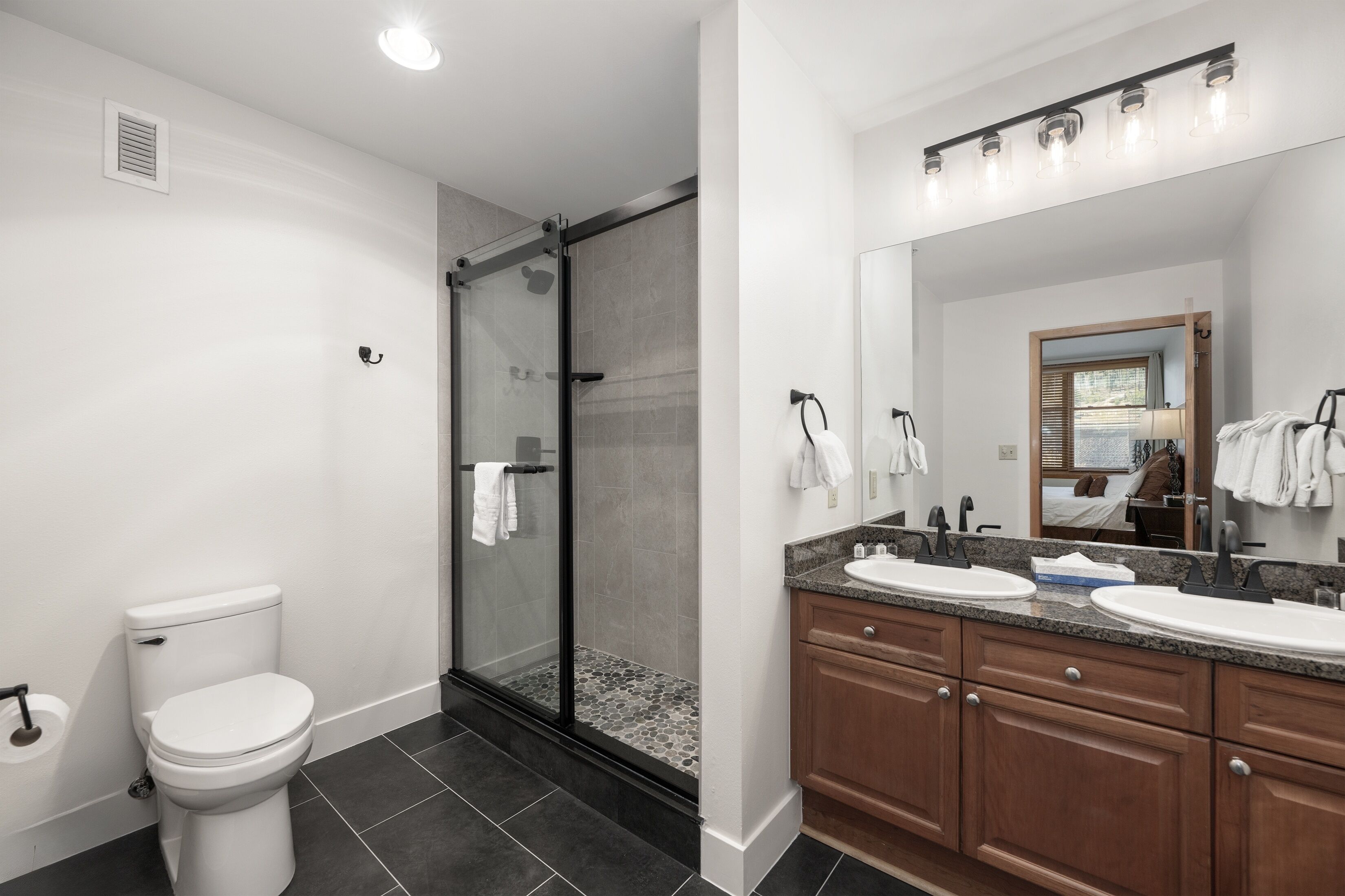 A modern bathroom with a toilet, shower, and vanity with a mirror.
