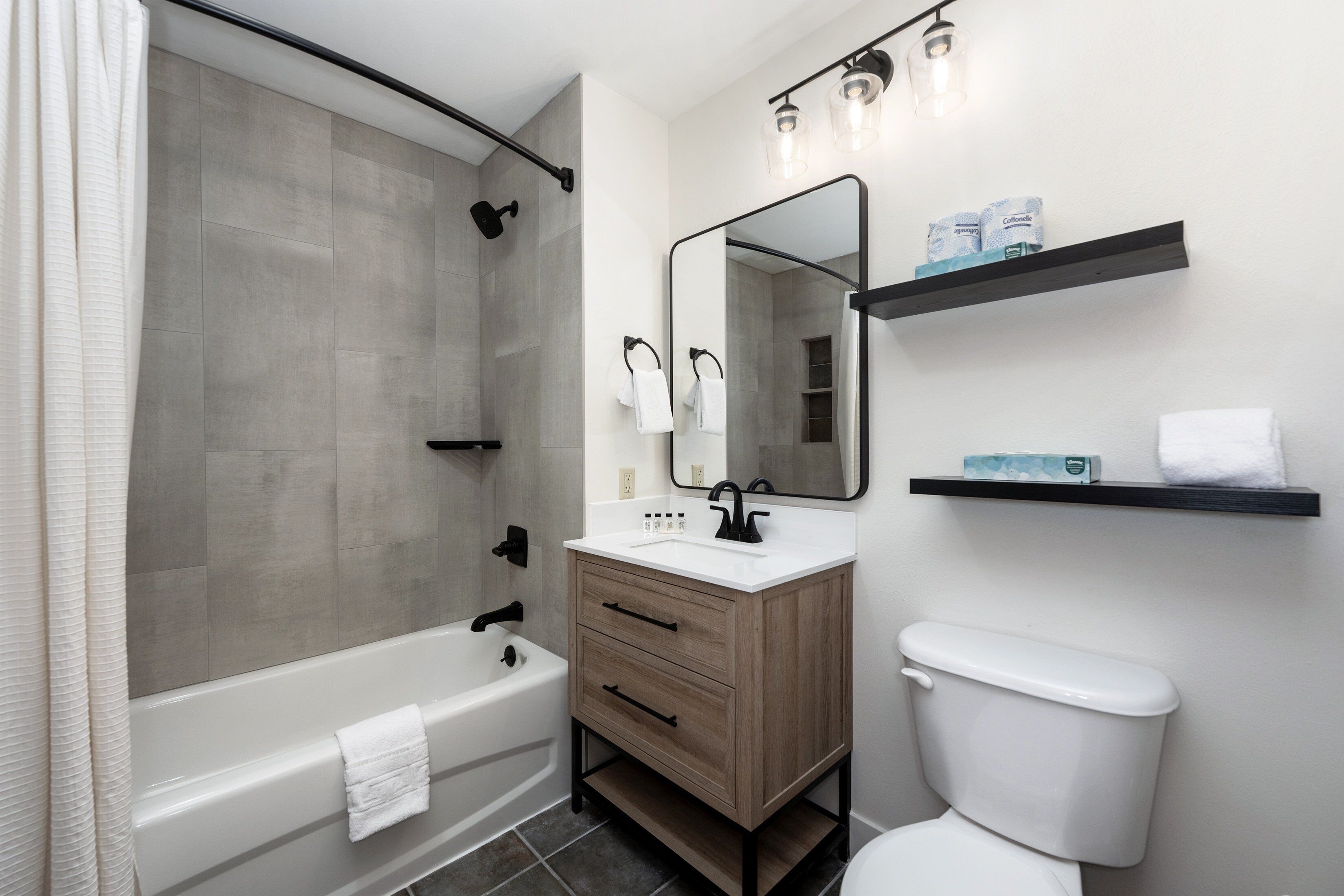 A modern bathroom with a bathtub, a toilet, a vanity with drawers, a mirror, and a shower area.