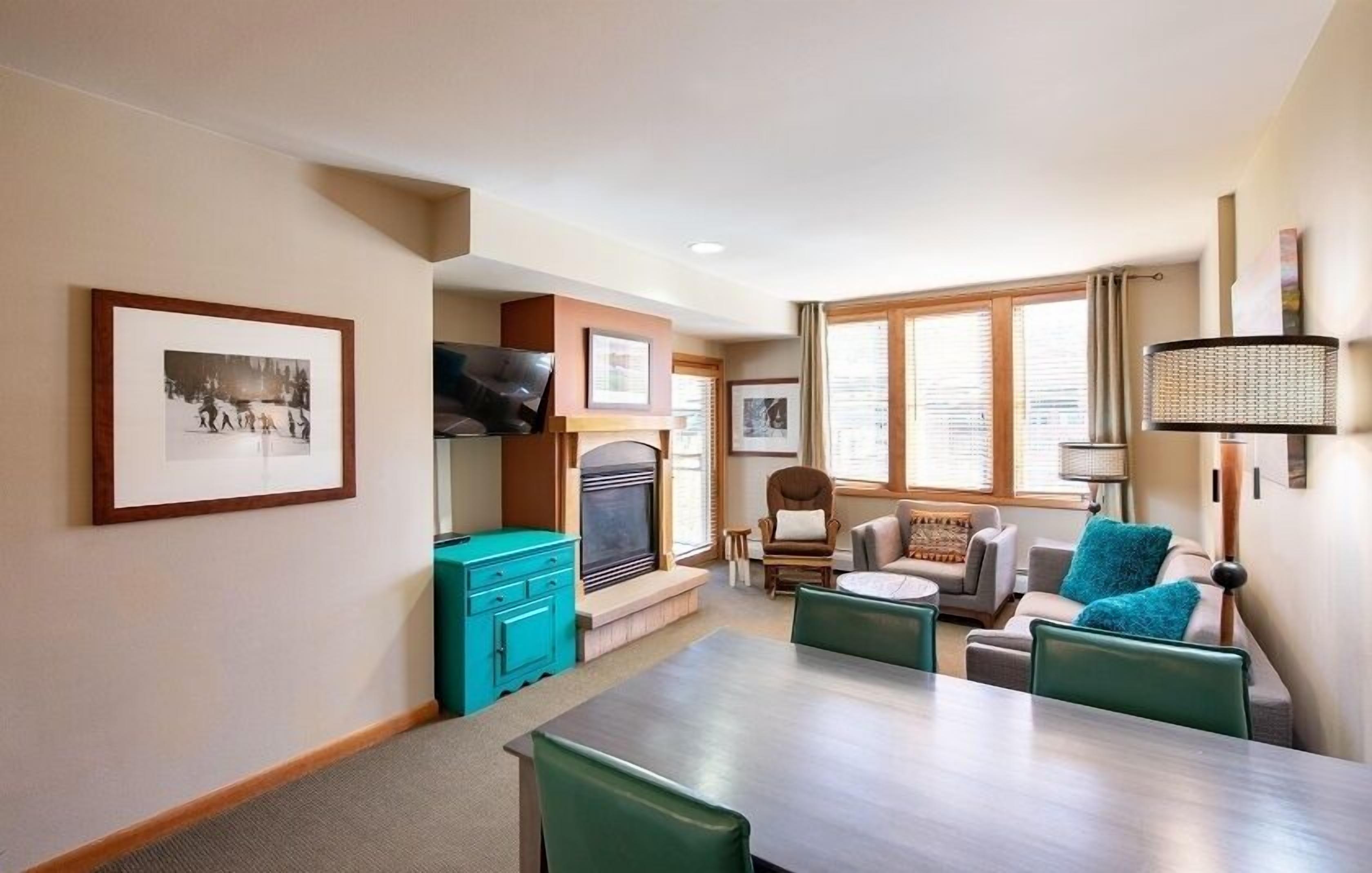 A modern living room with a fireplace, a television, and a dining area with green chairs.