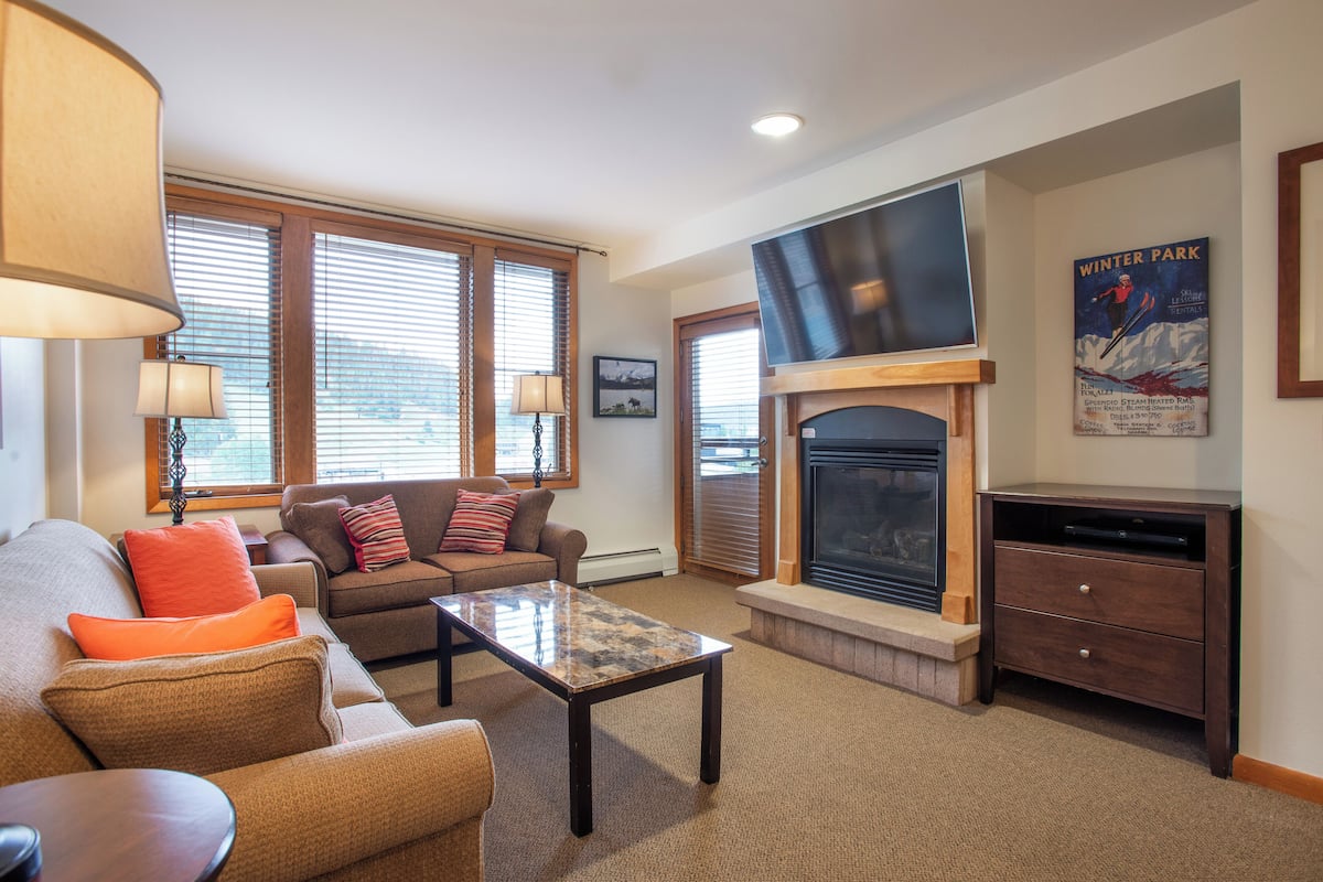 A cozy living room with a fireplace, a sofa with cushions, a coffee table, and a television.