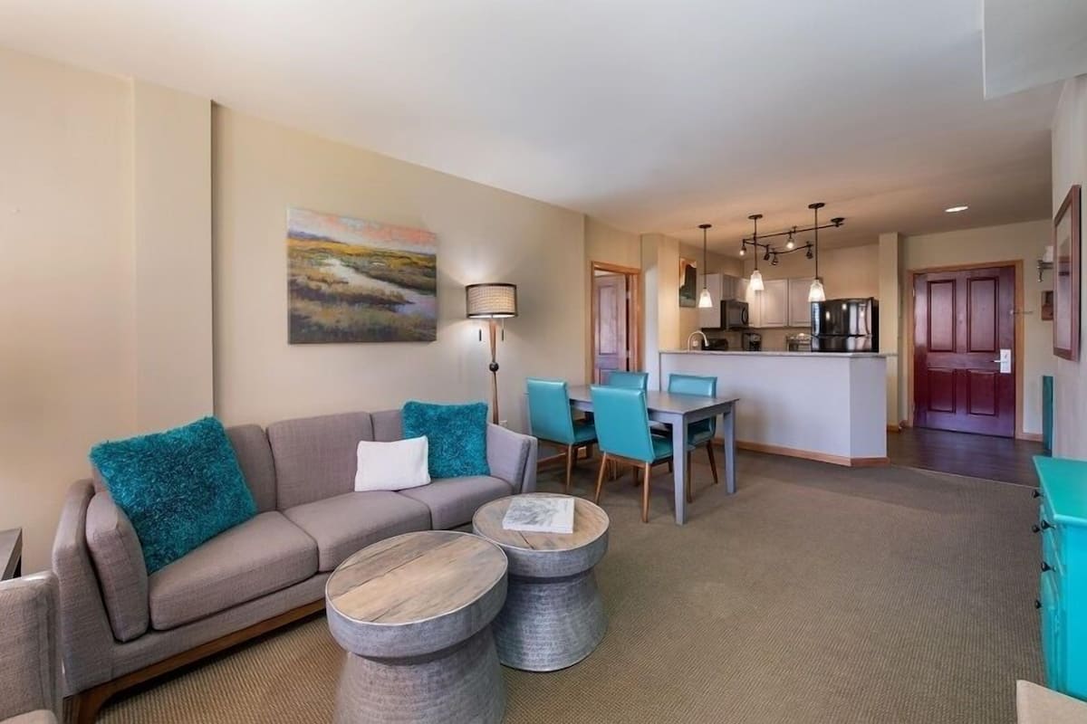 A modern living room with a sofa, two side tables, and a dining area with chairs and a table.