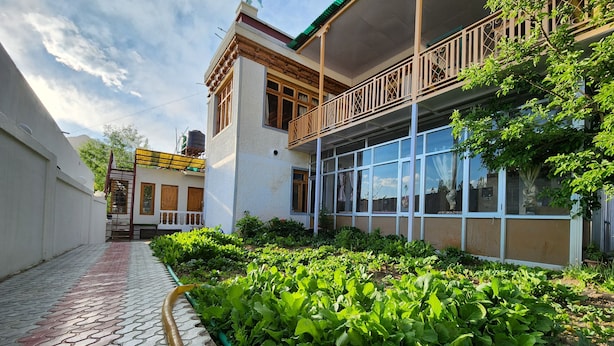A building with a garden area, a paved walkway, and a balcony. - Yanglha Guest House (Leh)