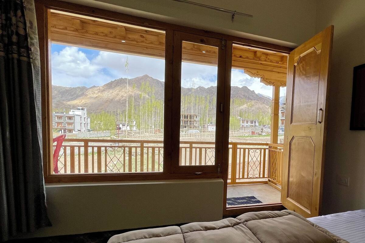 A bedroom with a large window, wooden balcony, and a bed.