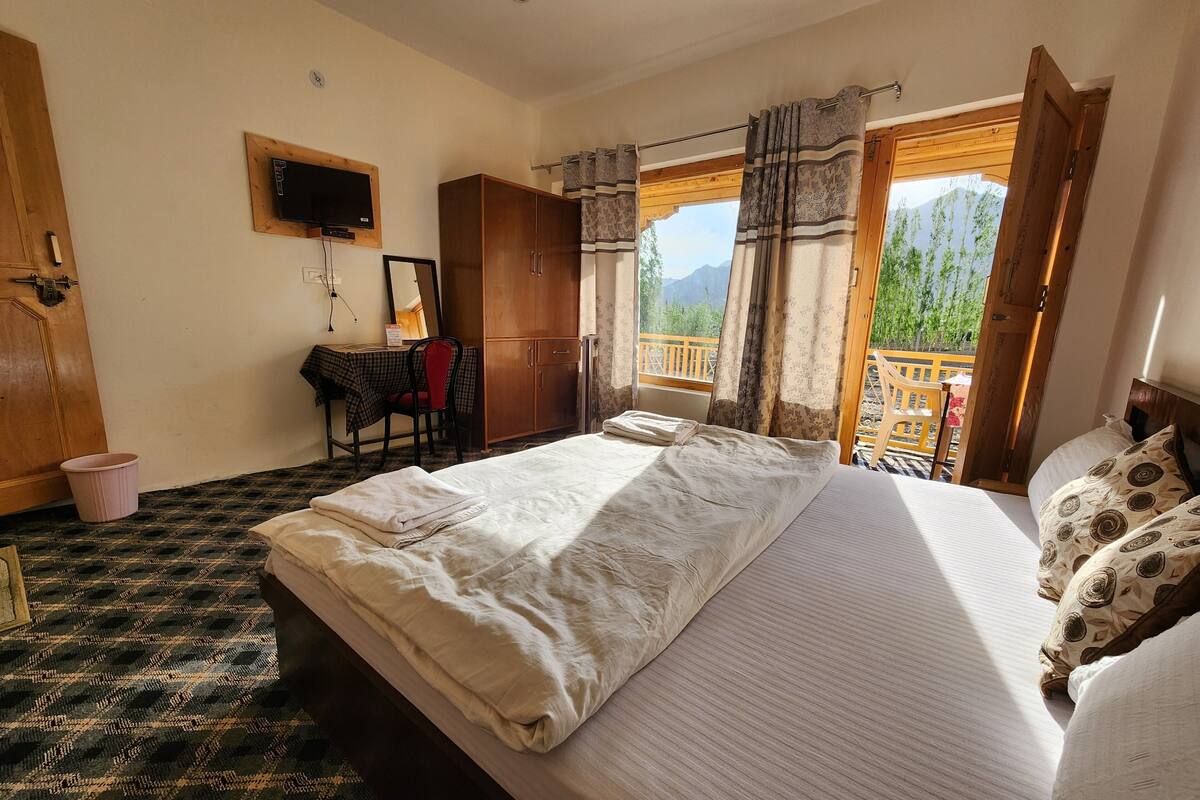 A bedroom with a bed, a desk, a chair, and a window with a view of mountains.