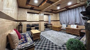 A cozy room with wooden walls and ceiling, a checkered rug, a sofa, a small table, and a decorative plant. - Yanglha Guest House (Leh)