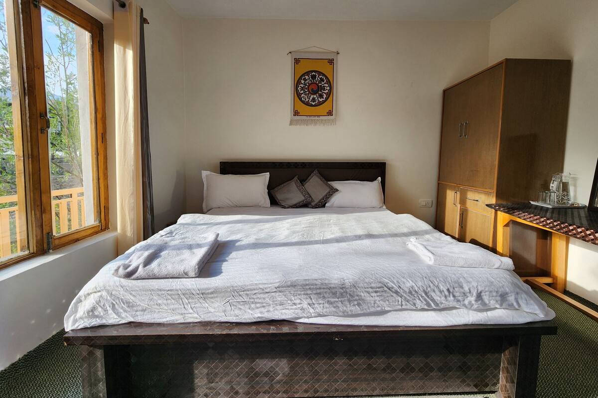A neatly made bed with white linens and towels, a wooden headboard, and a window with curtains.