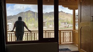 A room with a large window offering a view of a mountainous landscape and a person standing by the window. - Yanglha Guest House (Leh)