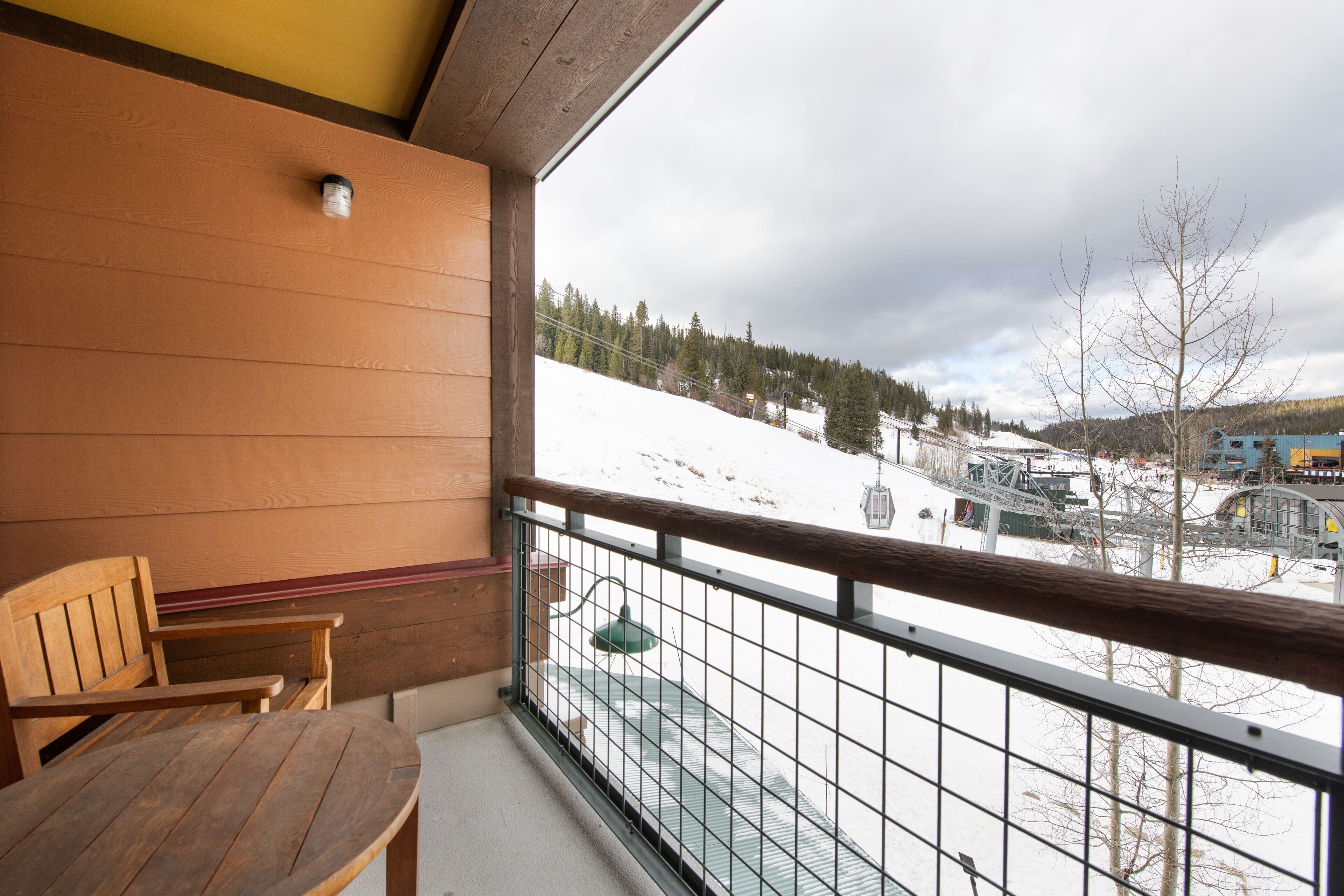 A wooden balcony with a view of a snowy mountain and ski lift.