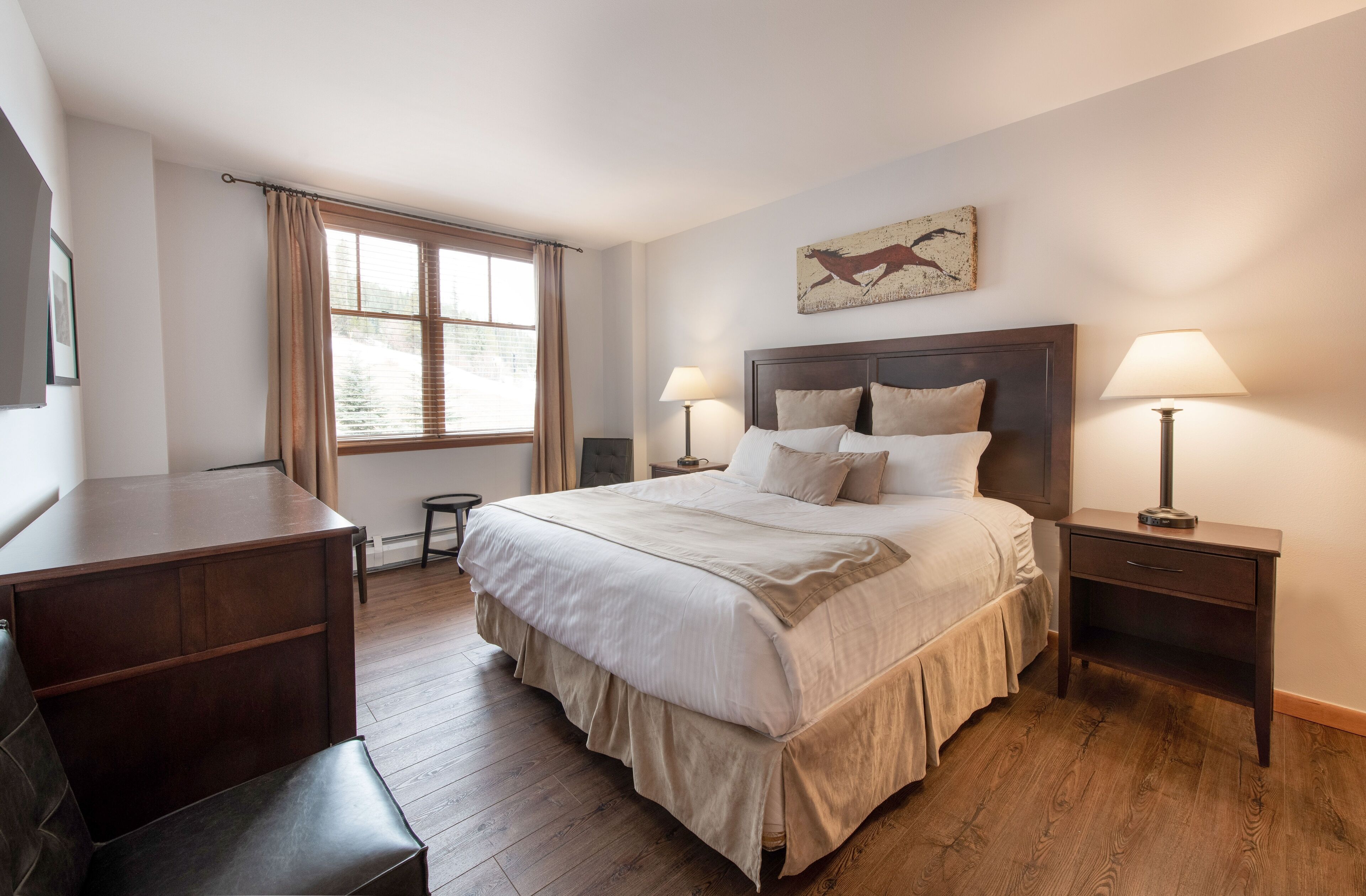 A bedroom with a large bed, bedside tables, a desk, and a window with curtains.