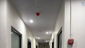 A hallway with patterned floor tiles, doors on both sides, and a fire alarm on the right wall. - Yatri Nivas By Sarvjeet Foundation (Varanasi)