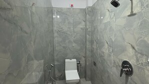 A modern bathroom with a glass-enclosed shower, a toilet, and a blue bucket. - Yatri Nivas By Sarvjeet Foundation (Varanasi)