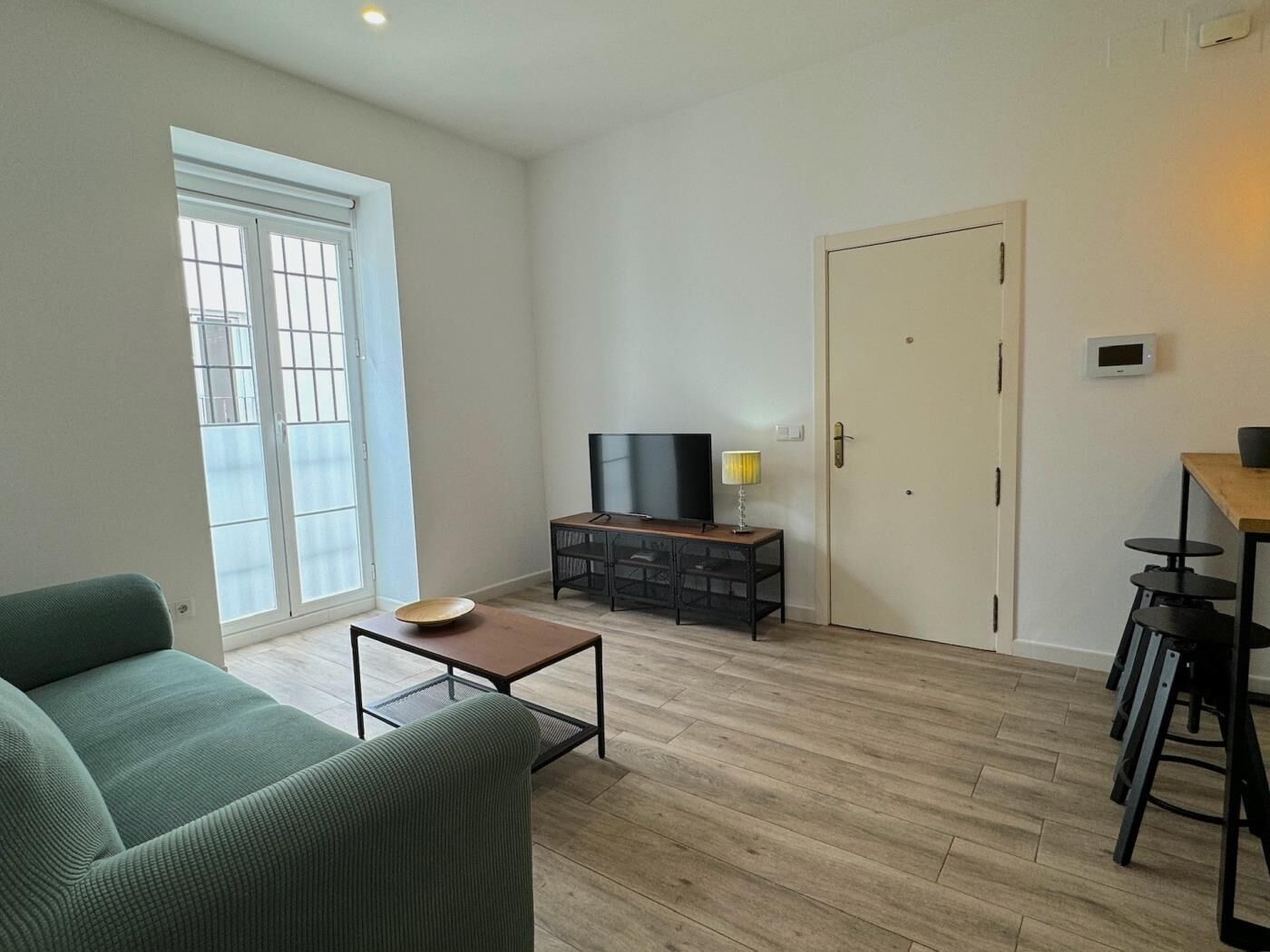 Un salon avec un canapé vert, une table basse, un téléviseur posé sur un meuble et une porte.