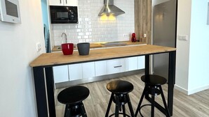 A modern kitchen with a wooden countertop, black stools, a stainless steel range hood, and a red kettle. - SibsSanLúcar Lucero 2 (Sanlucar de Barrameda)