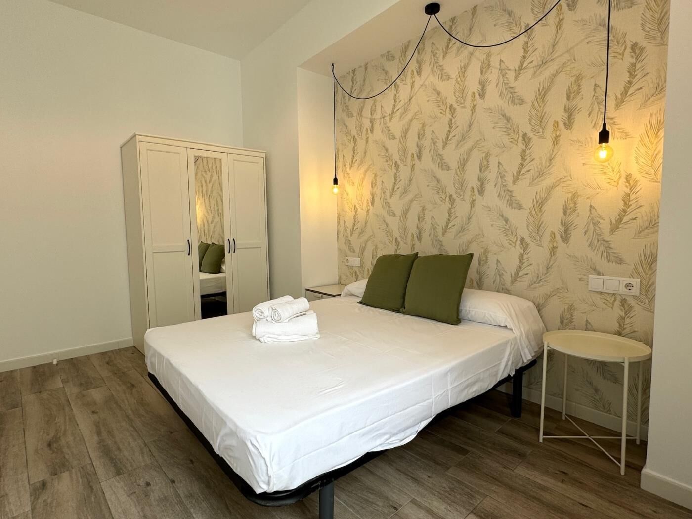 Une chambre à coucher comprenant un lit, une armoire, une table de chevet et un luminaire fixé au mur.
