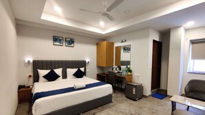 Une chambre d’hôtel moderne équipée d’un grand lit, d’un bureau, d’une chaise, d’une armoire et d’un ventilateur de plafond.