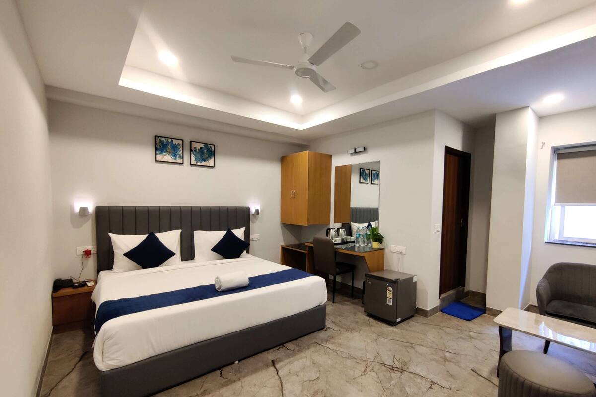 Une chambre d’hôtel moderne équipée d’un grand lit, d’un bureau, d’une chaise, d’une armoire et d’un ventilateur de plafond.
