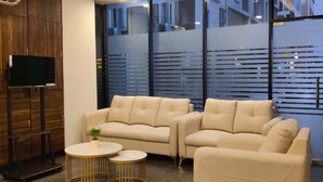 Un salon moderne avec un ensemble de canapés, deux petites tables rondes et un téléviseur posé sur un meuble en bois.