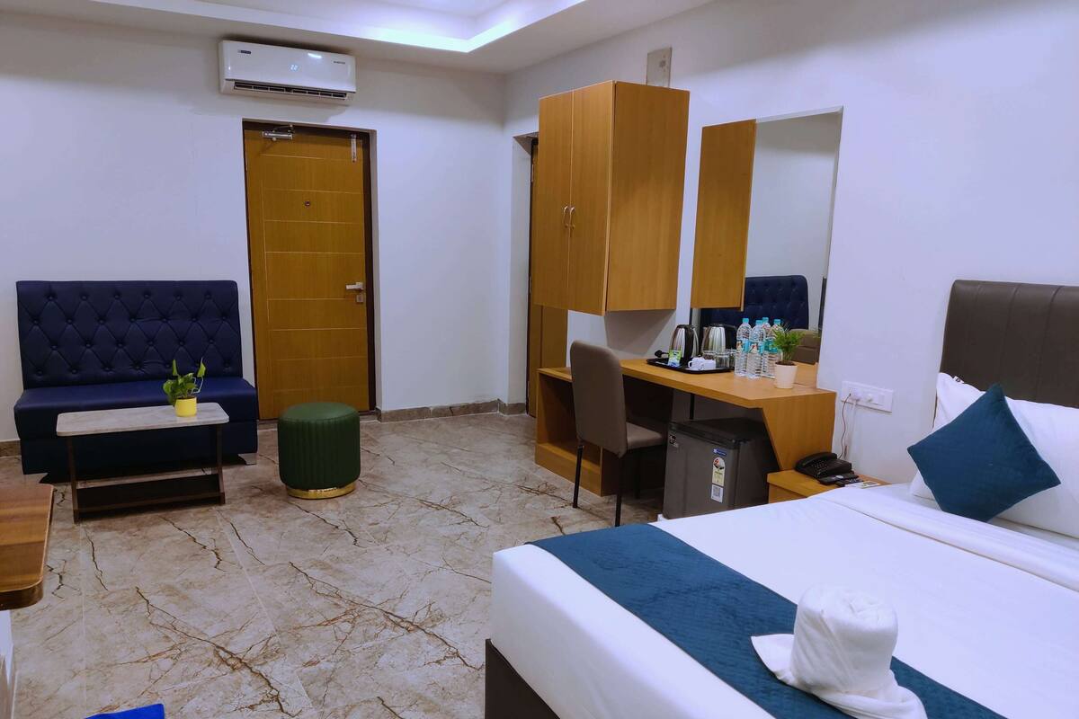 Une chambre d’hôtel comprenant un lit, un bureau, une chaise, un canapé, une petite table avec une plante et une armoire.