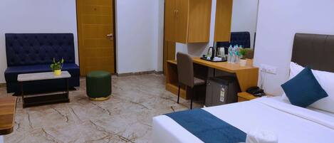 A hotel room with a bed, a desk, a chair, a sofa, a small table with a plant, and a wardrobe.