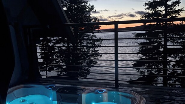 Un jacuzzi con vistas a la puesta de sol sobre una masa de agua, rodeado de árboles.