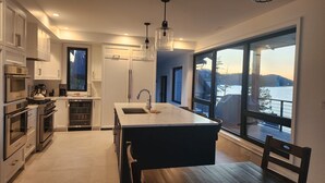 Eine moderne Küche mit einer zentralen Kochinsel, Edelstahlger äten und einem großen Fenster mit Seeblick.