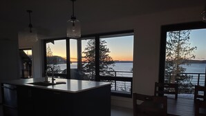 Una cocina moderna con una isla grande, ventanas amplias y vistas a un cuerpo de agua al atardecer.
