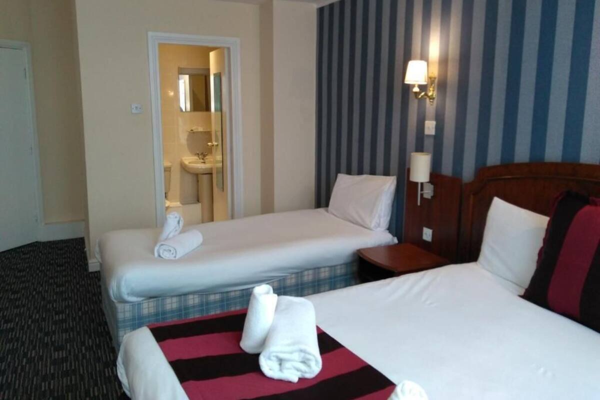 Quarto de hotel com duas camas de solteiro, uma cama de casal, banheiro com espelho e parede listrada.