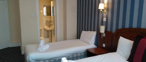 A hotel room with two single beds, a large bed, a bathroom with a mirror, and a striped wall.