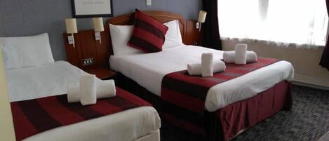 A hotel room with two beds, each with a red and black striped bedspread, white pillows, and white towels. There is a framed picture on the wall and a window with curtains.