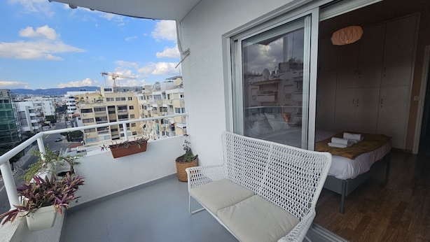 A balcony with a white wicker chair, a small table, and potted plants. - STAY Velvet Apartment (Limassol)