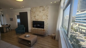 Un salon moderne doté d’un grand téléviseur, d’un canapé confortable, d’une table basse et offrant une vue sur la ville grâce à une grande fenêtre.