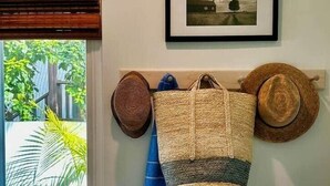 A room with a window overlooking greenery, a framed picture on the wall, and a woven bag hanging on a hook. - Soul & Sea #1 – East Beach Guesthouse (Santa Barbara)