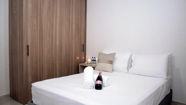 A hotel room with a bed, a nightstand, a bottle of champagne, and a wooden wardrobe. - Encantador apartamento nuevo de 1 dormitorio WiFi aire acondicionado Cartagena (Cartagena de Indias)