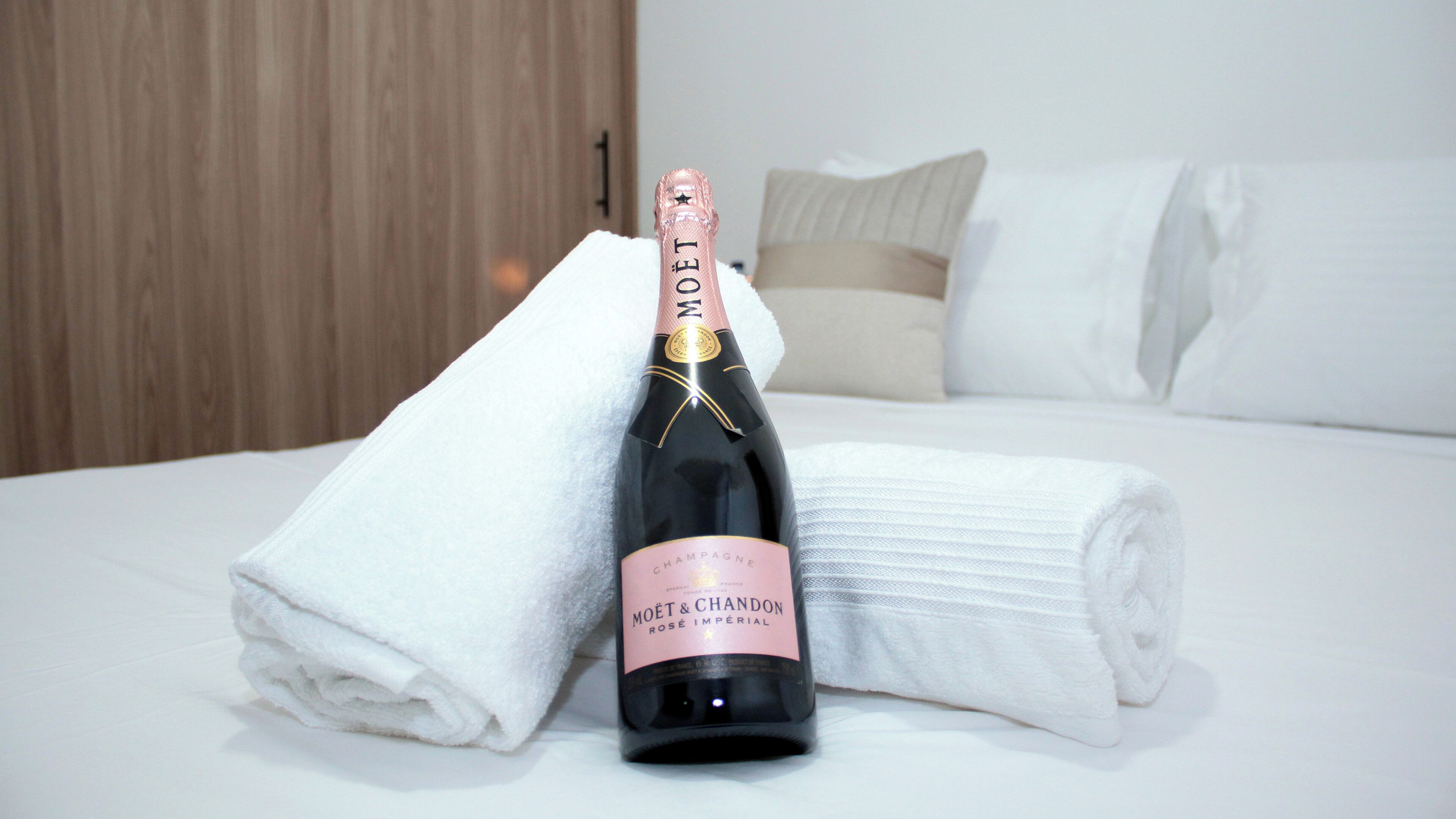 A bottle of Moët & Chandon champagne on a bed with white linens and a folded towel.