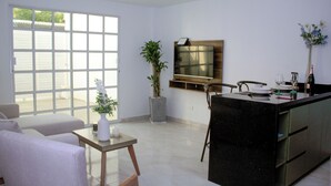 A modern kitchen with a black countertop, a dining area with a white sofa, a small table with a vase, and a large window with blinds. - Encantador apartamento nuevo de 1 dormitorio WiFi aire acondicionado Cartagena (Cartagena de Indias)