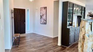 A spacious hallway with wooden flooring, a dark door, and a modern chandelier. - Elevated Elegance with Golf Course Access & Panoramic Valley Views (Hamilton)