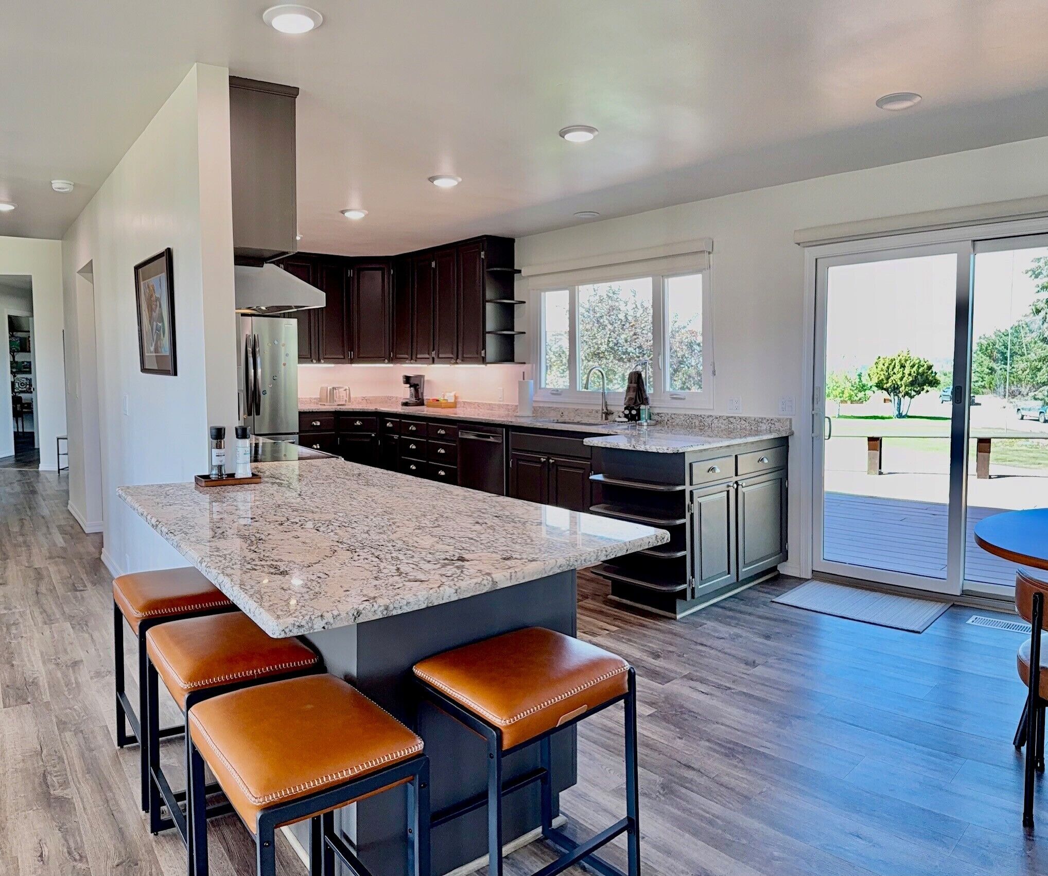 A modern kitchen with dark cabinets, a granite island, and a dining area with leather stools.