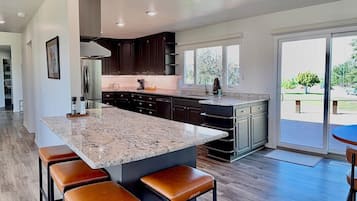A modern kitchen with dark cabinets, a granite island, and a dining area with leather stools.