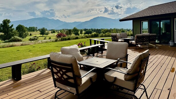 A deck with outdoor furniture overlooking a scenic landscape with mountains. - Elevated Elegance with Golf Course Access & Panoramic Valley Views (Hamilton)