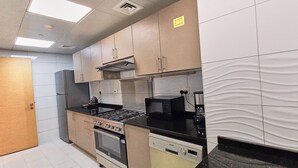 A compact kitchen with a gas stove, oven, microwave, and a built-in range hood. - Royal Home Deluxe Apartments, Beach View, 5min to Corniche (Abu Dhabi)