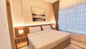 A hotel room with a large bed, nightstands, a lamp, a painting, and a view through sheer curtains. - Royal Home Deluxe Apartments, Beach View, 5min to Corniche (Abu Dhabi)