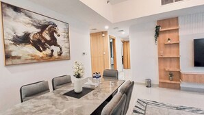 A modern dining area with a marble table, grey upholstered chairs, a large abstract painting, and a flat-screen TV mounted on a wooden wall. - Royal Home Deluxe Apartments, Beach View, 5min to Corniche (Abu Dhabi)